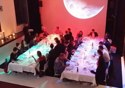 A large group of people seated at tables with elegant lighting, enjoying dinner.